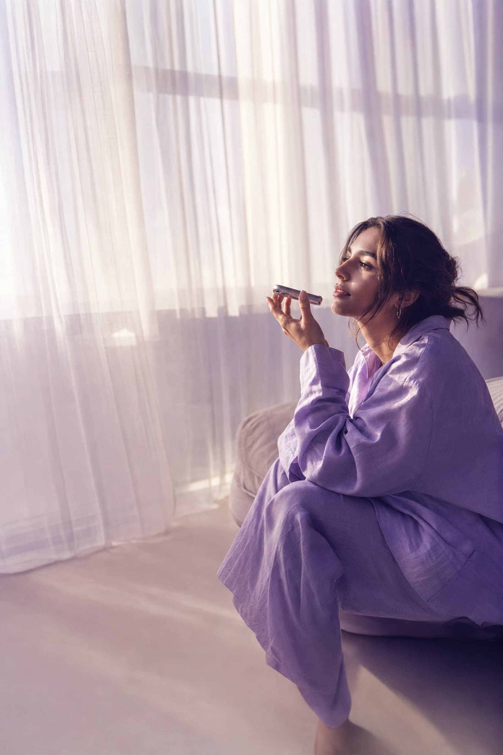 A high-key lavender morning: sheer curtains catch the light while someone speaks a quiet voice note.